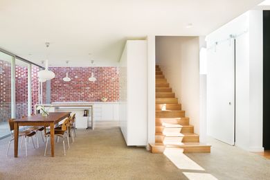 The imperfect red surfaces of the bricks provide a warm counterpoint to the white walls and joinery in the kitchen, dining and living zones. The enclosed stair leads to the bedrooms above.