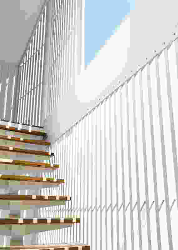 The white battened facade of the studio peels away from the building walls to allow for an open stair.