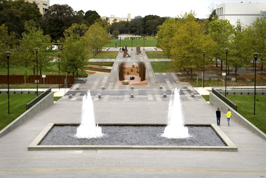 The campus and Reconciliation Place viewed from the NLA podium. Questacon is visible on the right and the NGA view corridor is revealed through the removal of Enid Lyons Street and transplanting of some 30 mature Plane Trees. The NLA water feature was restored to match its former glory. 