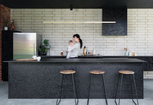 A kitchen in black oriented strand board (OSB) adds texture and tonal contrast to the white brick wall and light-filled courtyard opposite.