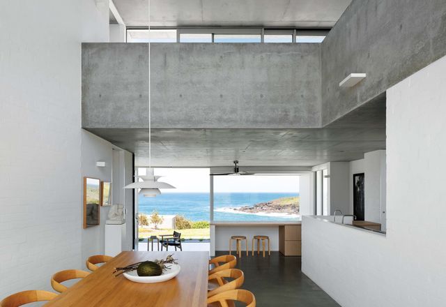 The coastal home is presented as a solid form, anchored to and growing up from the rock beneath it.