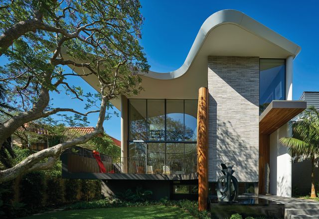 Otherwise rectilinear in form, the house features a curved roof and balcony that trace the canopy of a large jacaranda tree. Sculpture: Blaze Krstanoski-Blazeski.
