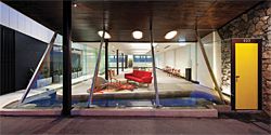 Projecting out beyond the front window, a yellow door offers a single point of solidity within the otherwise transparent facade.