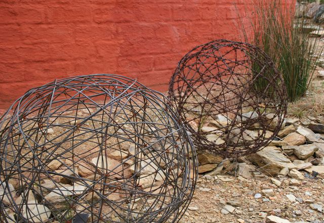 Old fencing wire used for sculptures in front of mudbrick wall.