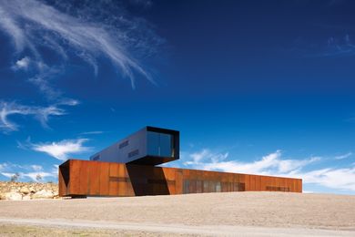 A Corten block is set athwart the hill, with the black upper floor sitting at a right angle across it.