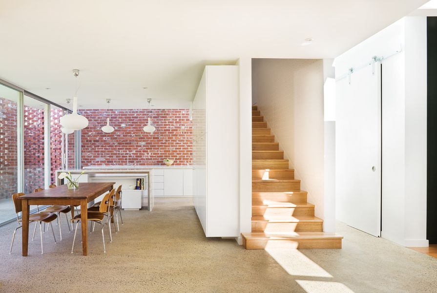 The imperfect red surfaces of the bricks provide a warm counterpoint to the white walls and joinery in the kitchen, dining and living zones. The enclosed stair leads to the bedrooms above.