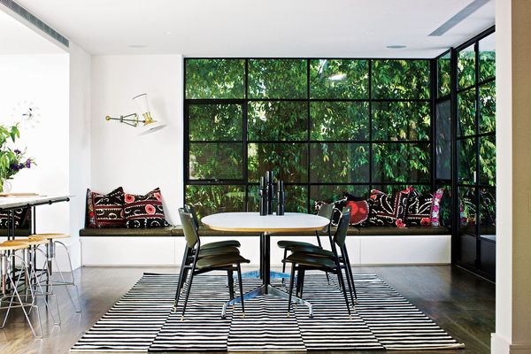 A window seat stretches along the northern edge of the dining room, with a multi-paned window framing a wall of greenery outside.