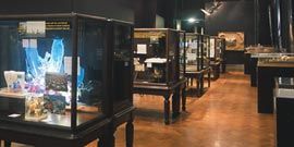 The exhibition installed at the Victoria and Albert Museum. A row of paired Victorian display cases stretching toward the end wall, on which Gregory Burgess Architects’ model of the Brambuk Living Cultural Centre is displayed.