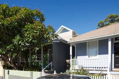 The gable-roofed addition floats above the modest single-storey brick and green weatherboard cottage.