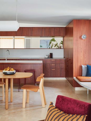 White ceramic benchtops act as a palate cleanser beside the dominant rust-coloured timber tones in the kitchen.