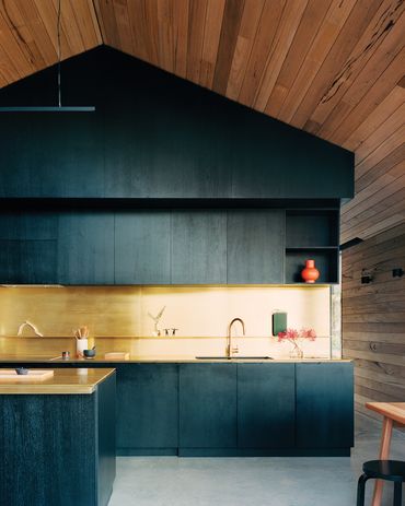 Bright brass kitchen surfaces contrast sharply with the blackened timber joinery.