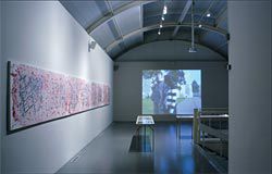 Overview of the
upper-level exhibition
space seen from the
pavilion entry, with
Louise Forthun’s
painting to the left and
one of the two thematic
video loops at the rear.