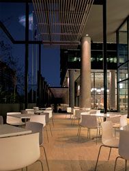 Outdoor cafe, looking towards the courtyard. The outdoor spaces are designed as an extension of the indoor communal facilities. The horizontal sunscreens protect the podium facades from solar heat gain and define the cafe seating area.