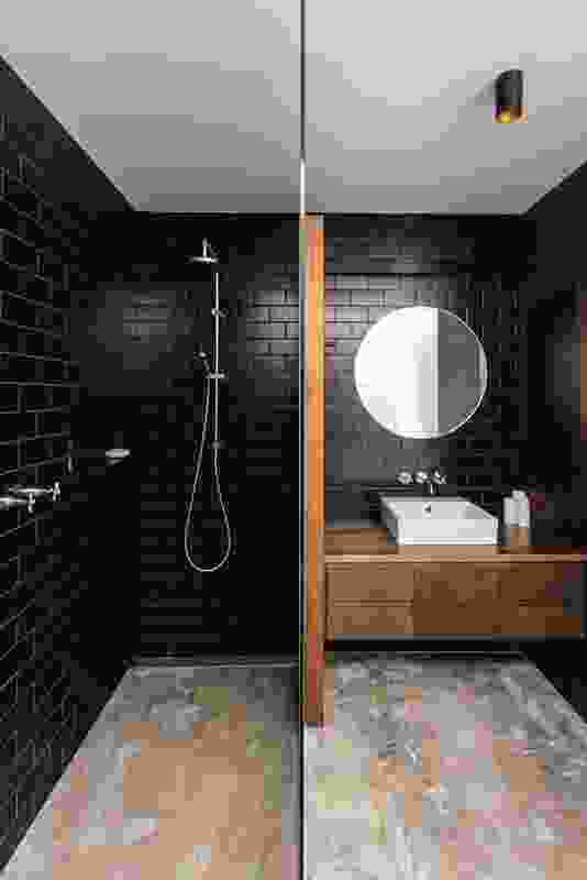 Dark wall tiles in the bathroom are balanced by the softer tones of the concrete floors and timber joinery.